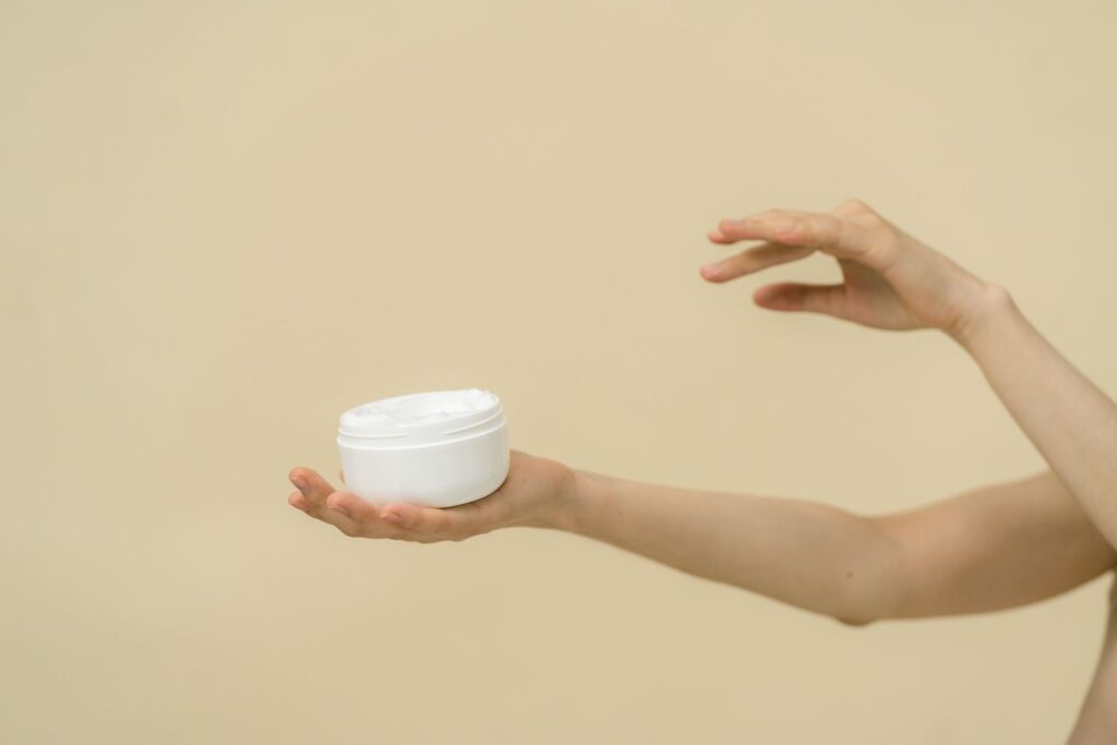 Glicerina no rosto: mão segurando pote de creme hidratante