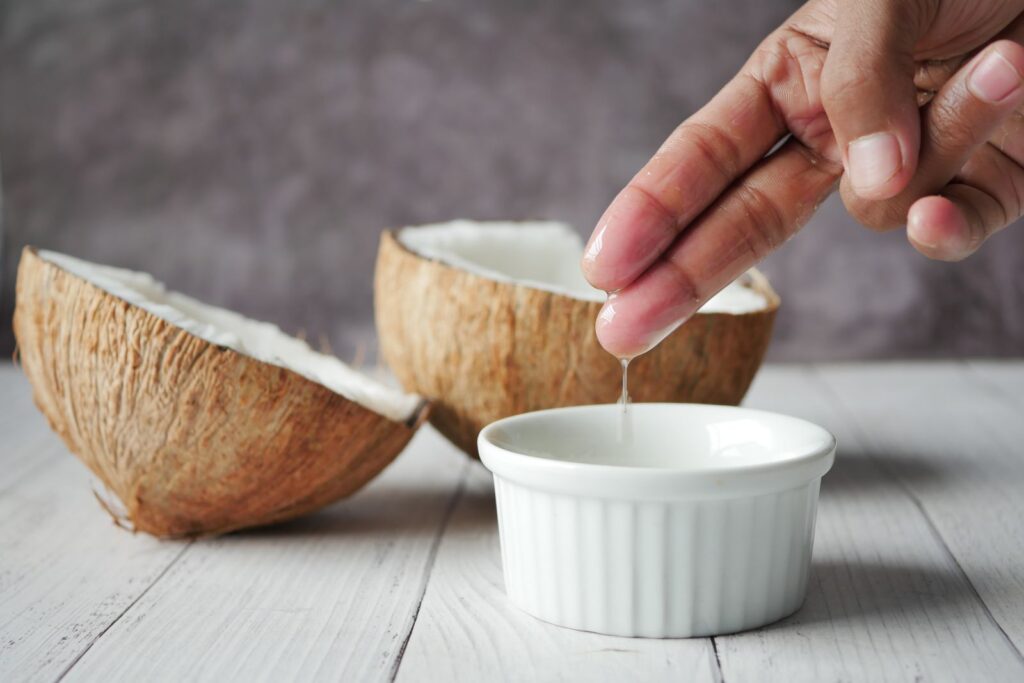 Óleo de coco no rosto: óleo escorrendo em tigela ao lado de coco aberto