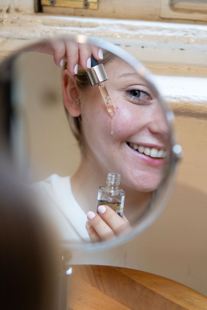 Mulher sorrindo no espelho enquanto aplica sérum facial na rotina da noite