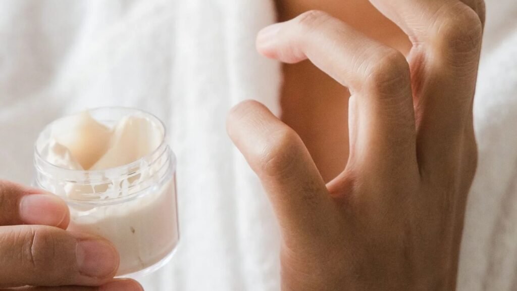 Ceramidas ou ácido hialurônico: mão segurando pote de creme hidratante aberto (imagem ilustrativa)