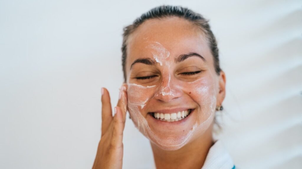Imagem ilustrativa sobre como escolher protetor solar Principia: mulher espalhando creme branco no rosto